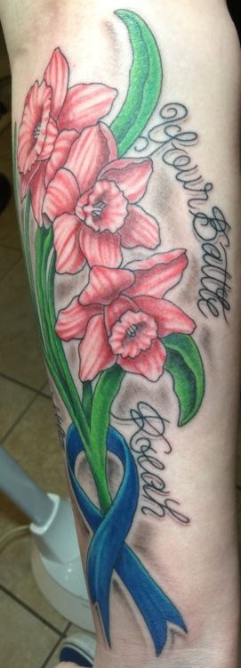 Tattoo of pink daffodils, blue ribbon, and names on a person's arm.