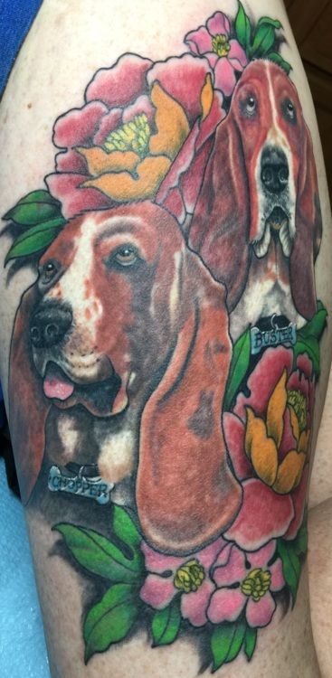 Tattoo of two Basset Hounds with pink and yellow flowers on a person's skin.