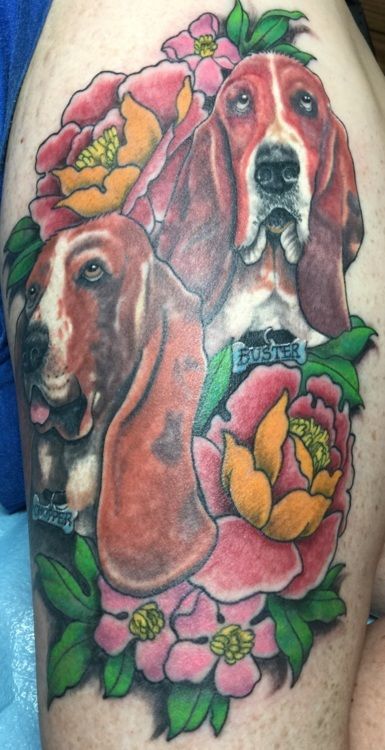 Tattoo of three Basset Hound faces surrounded by vibrant pink and yellow flowers on skin.