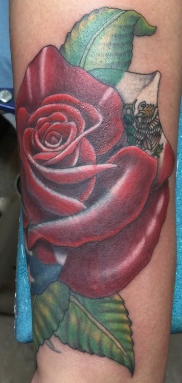 Tattoo of a vibrant red rose with green leaves on a person's arm.