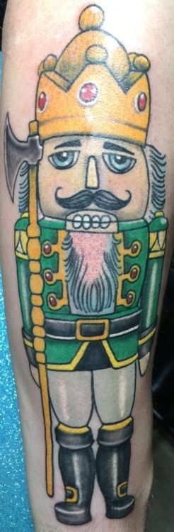 Tattoo of a green and gold nutcracker in a crown holding an axe.