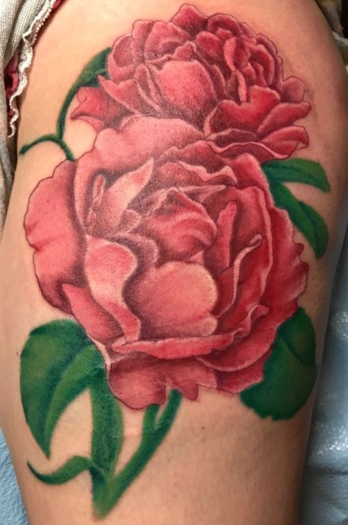 Tattoo of two red peony flowers with green leaves on skin.