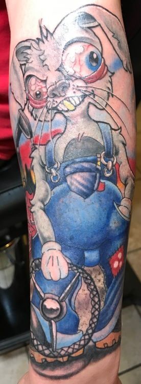 Tattoo of a crazed rabbit driving a car. The rabbit has bloodshot eyes and a wild grin. The driver is in blue overalls.