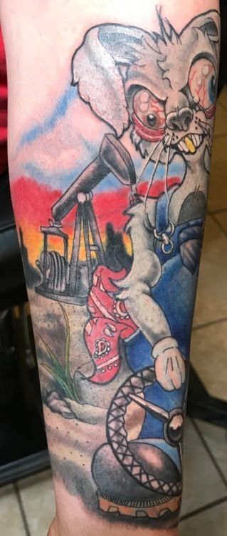 Tattoo of a cartoon rabbit driving, with an oil rig in the background, set against a red and blue sky.