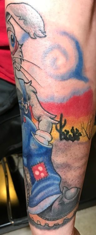 Tattoo of Bugs Bunny wearing a blue outfit in a desert setting with a red sky and cacti.