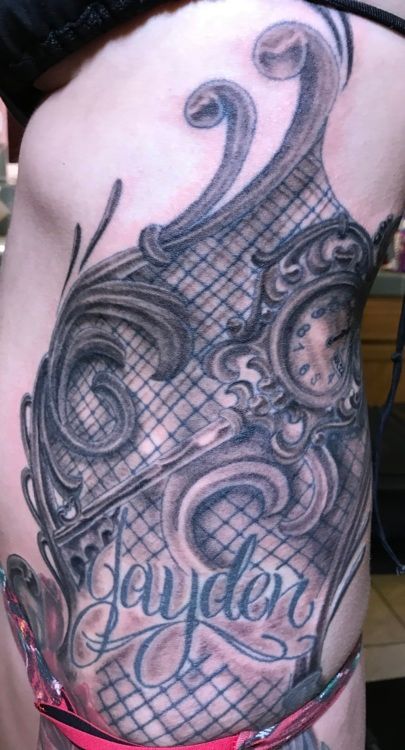Tattoo on body with ornate scrollwork, a clock, and the name 