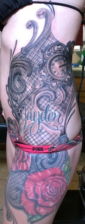 A side view of a person's torso and thigh with an intricate tattoo, featuring a clock, name 