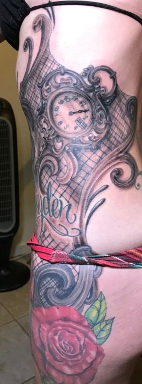 Tattoo of a clock, ornate scrollwork, and a rose on a person's side and thigh.