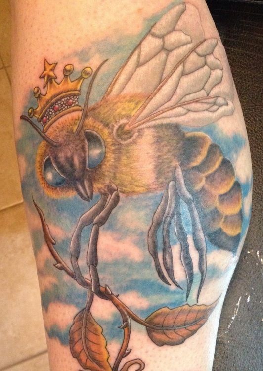 Tattoo of a bee wearing a crown, perched on a branch, with blue and white clouds in the background.