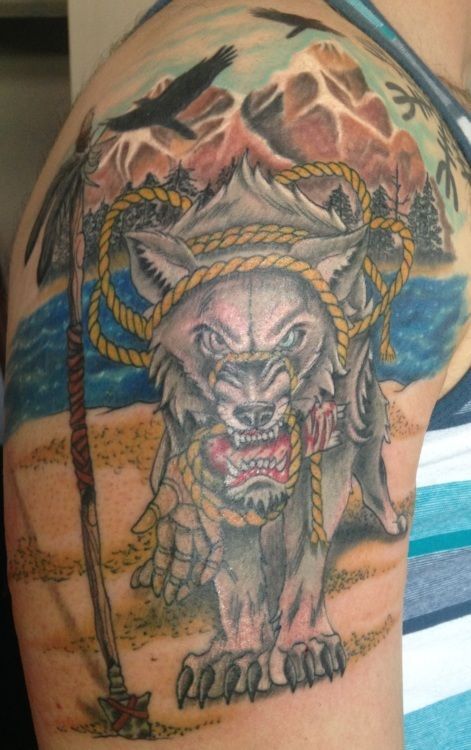 Tattoo on shoulder of snarling wolf bound by rope, mountain range background, crows flying.