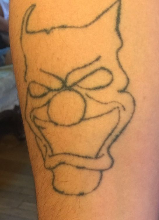 Outline of a clown face tattoo with horns, angry eyes, and a large smile.
