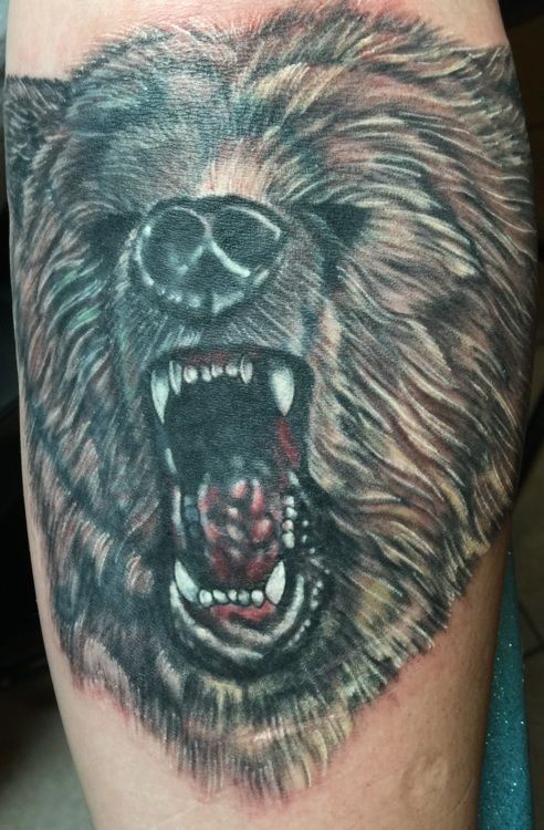 Close-up tattoo of a roaring bear's head, showing teeth and snarling expression, with brown fur.