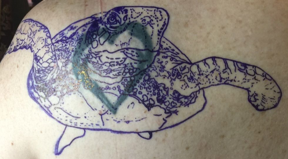 Blue outline of a sea turtle tattoo design on a person's back, with a light green design in the turtle's body.