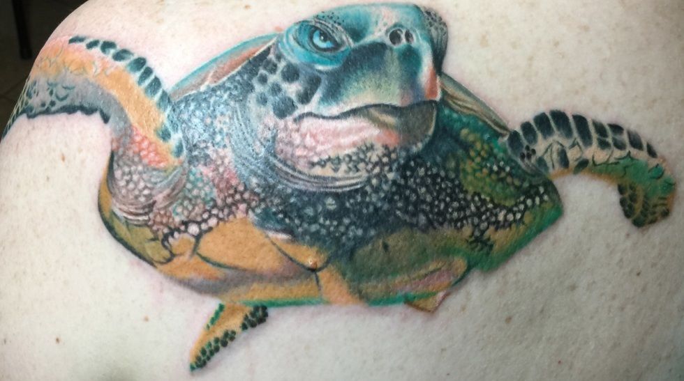 Colorful tattoo of a sea turtle on a shoulder, featuring blues, greens, yellows, and detailed shading.