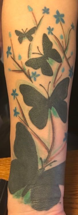 Arm tattoo of dark butterflies and blue flowers on a light skin tone.