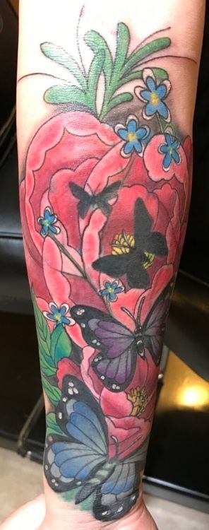 Tattoo of a vibrant red flower and butterflies in shades of purple and blue on an arm.