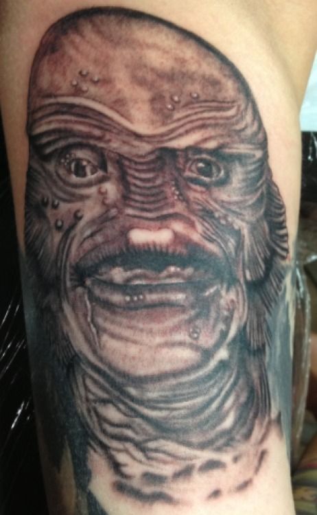 Creature from the Black Lagoon tattoo in grayscale on an arm. Close-up of the monster's face with a neutral expression.