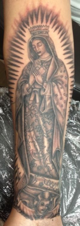 Tattoo of the Virgin Mary on an arm, in grayscale, with a halo and crown.