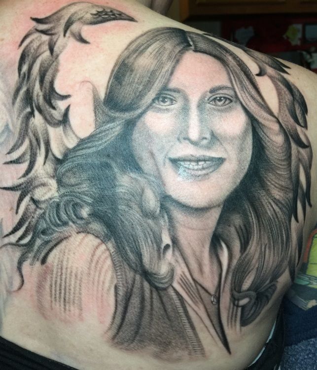 Black and white tattoo on a person's back; woman's portrait with flowing hair, with a design beside her face.