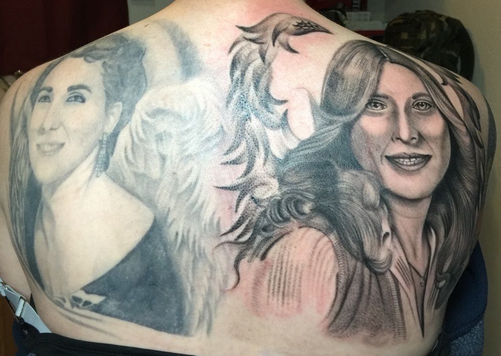 Tattoo on a person's back featuring two portraits and a winged design between them.
