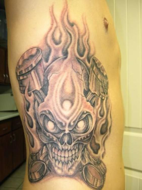 Tattoo of a skull engulfed in flames on a person's side; gray and white shading.