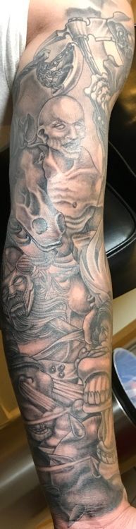 Tattoo of skulls and faces with flowing, detailed black shading on a person's arm.