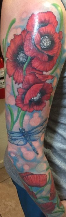 Tattoo of red poppies and a blue dragonfly on an arm. Green stems and blue background.