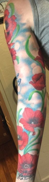 Arm tattoo of red poppies, green stems, and blue sky.