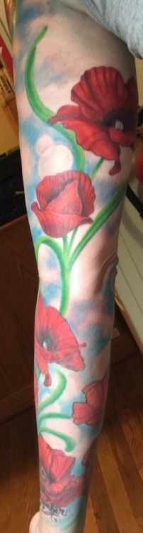Leg tattoo of red poppies with green stems on a cloudy blue background.