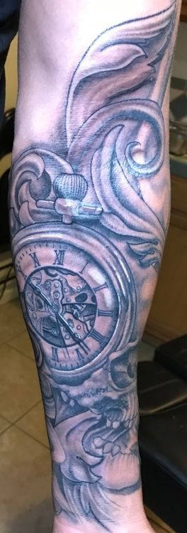 Tattoo of a pocket watch with Roman numerals and ornate swirls on a forearm. Black and gray shading.