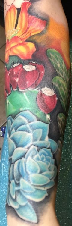 Tattoo of colorful flowers and succulents on an arm, with blue, red, orange, and green hues.