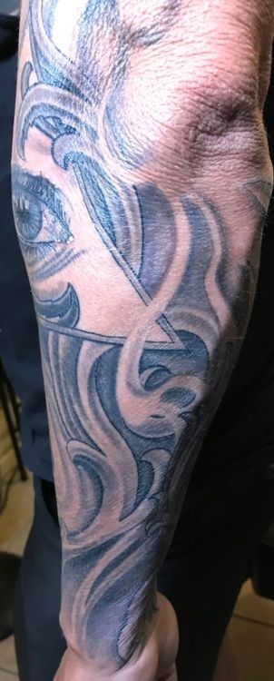 Tattoo of eye and abstract design on forearm; gray and white tones.