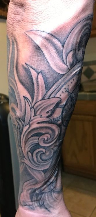 Black and gray tattoo on an arm, featuring ornate swirls and floral designs.