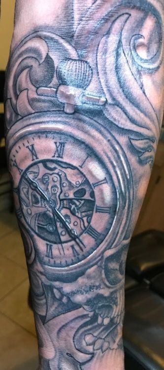 Tattoo on an arm, featuring a pocket watch design with roman numerals, set in ornate swirls.
