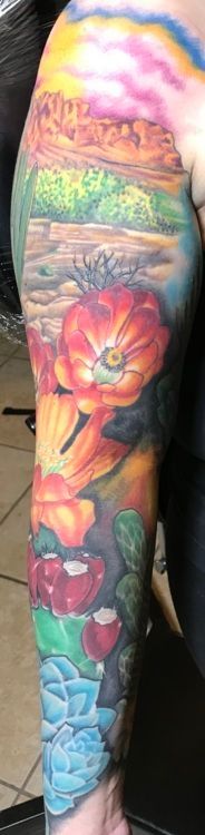 Colorful arm tattoo featuring a landscape, large flower, lips, and aquatic plant designs.