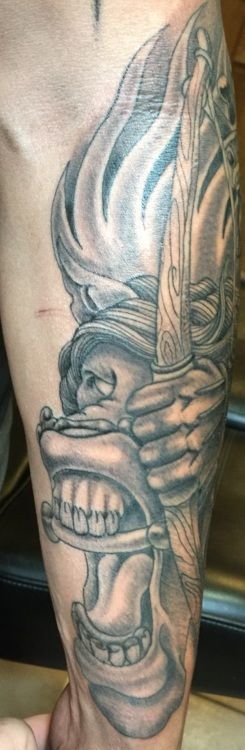 Tattoo on an arm. It shows a human skull holding a dagger, with smoke around the head and face.