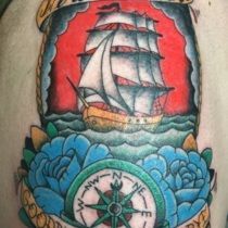 Tattoo of a ship sailing on the sea with a compass and blue roses. Red, yellow, blue, and black.