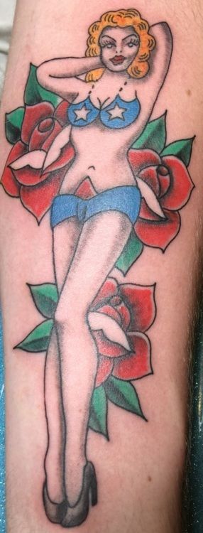 Tattoo of a woman in a blue bikini and high heels, posed between two red roses.