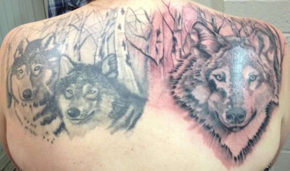 Tattoo on a back, featuring three wolf heads with detailed fur, set in a birch forest design.
