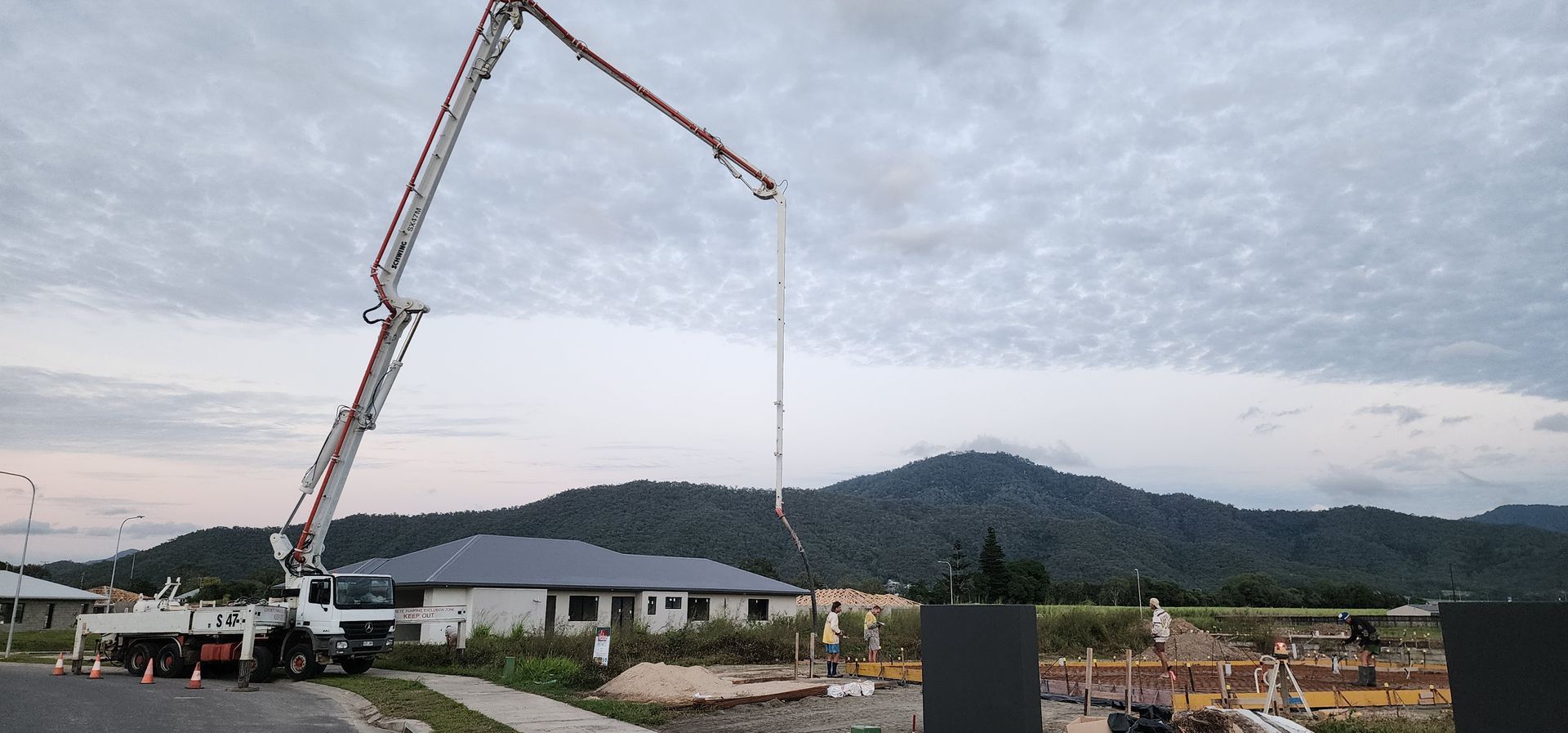 Crane lifting a load near a construction site with mountains and cloudy sky in the background
