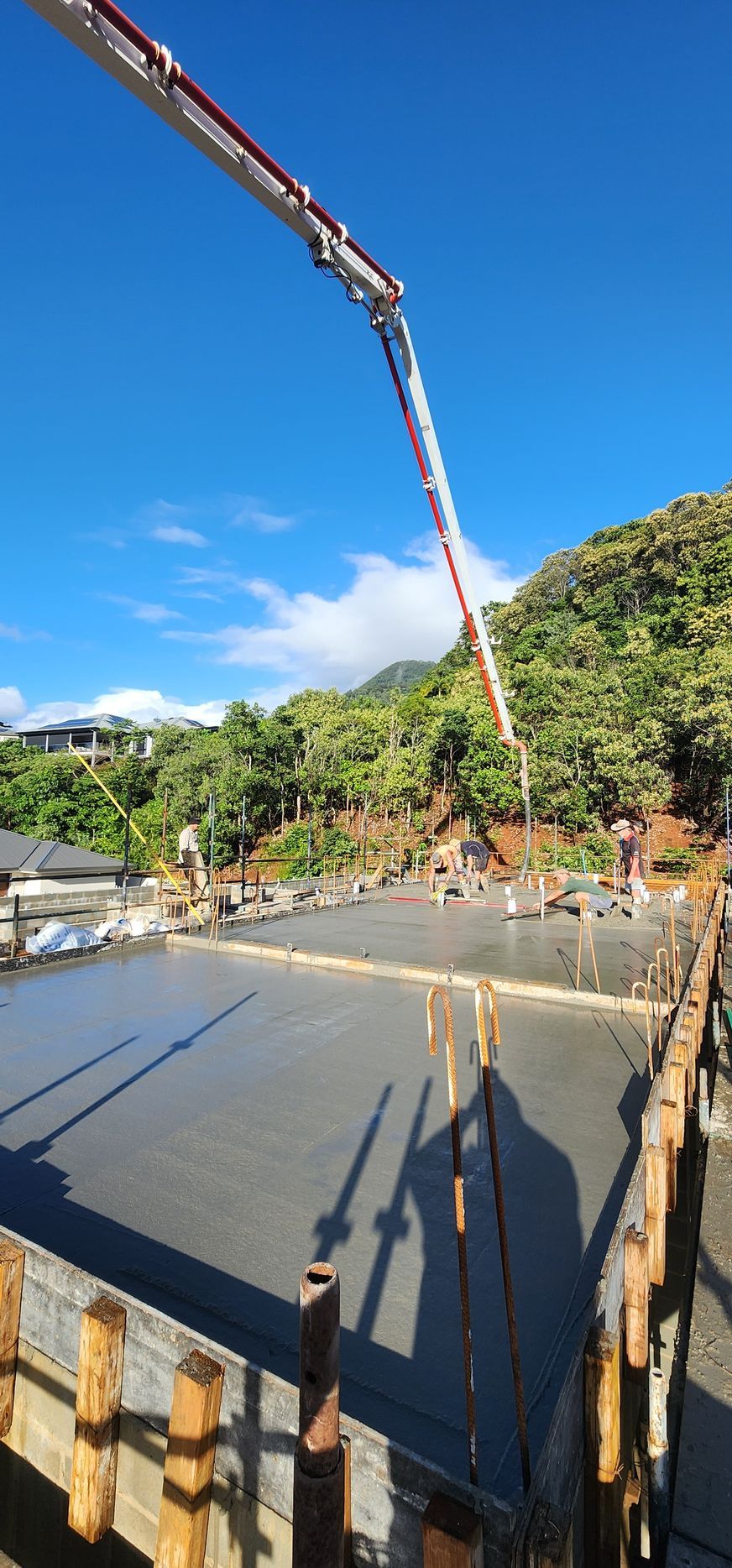 Construction site with concrete slab, rebar, and a long boom pump pouring concrete outdoors.