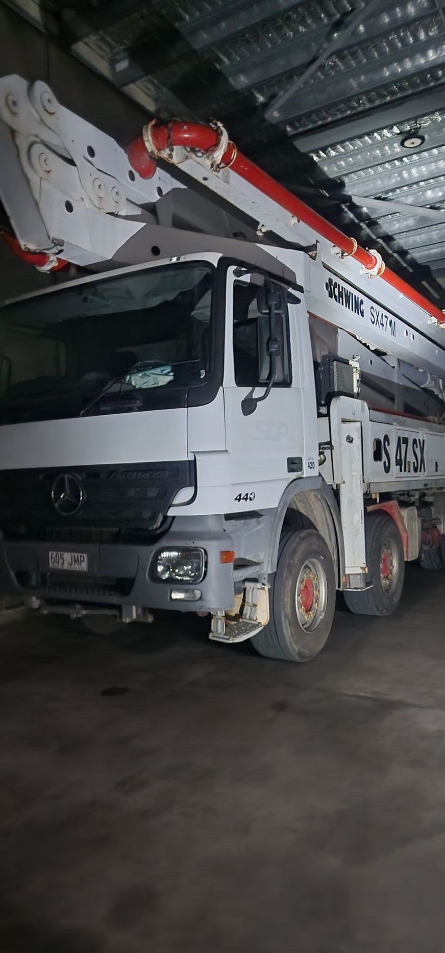 White concrete mixer truck with red boom parked inside a warehouse garage