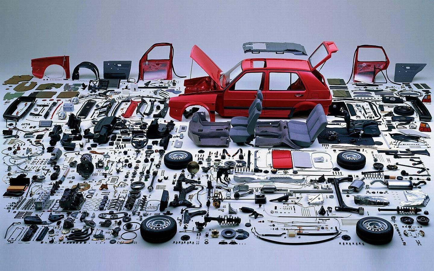 Red car disassembled with parts spread on a white surface, showcasing components of a vehicle.