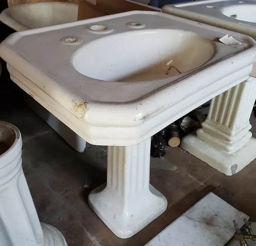 A white pedestal sink sits on a wooden floor