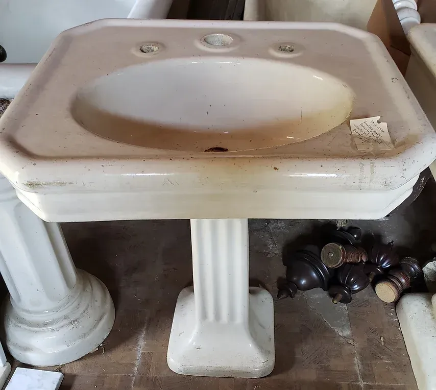A white pedestal sink sits on a tiled floor