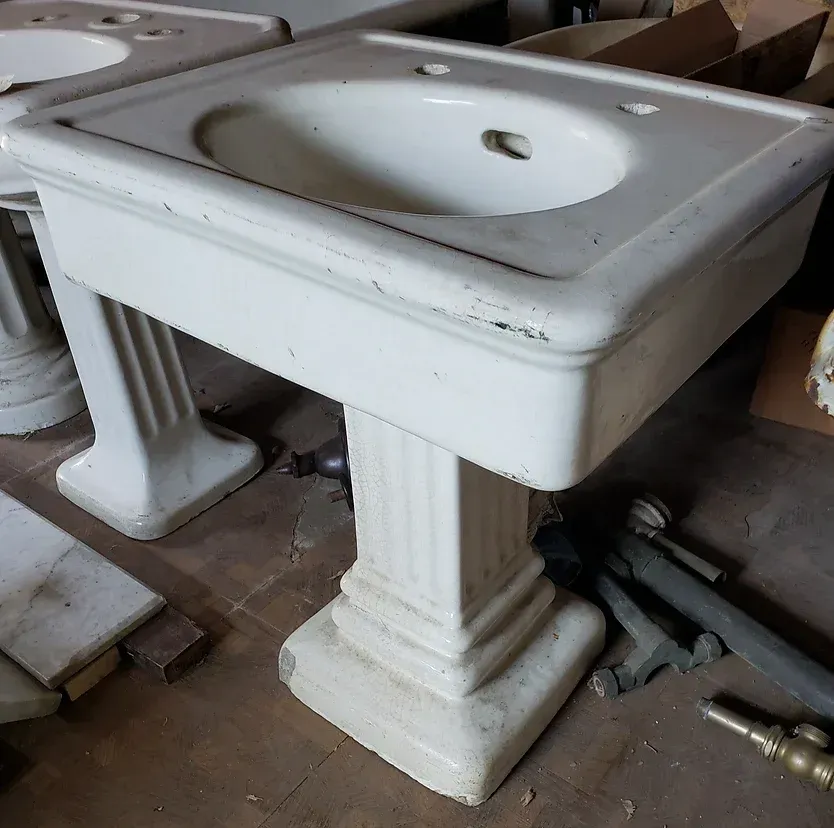 A white pedestal sink sits on a wooden floor