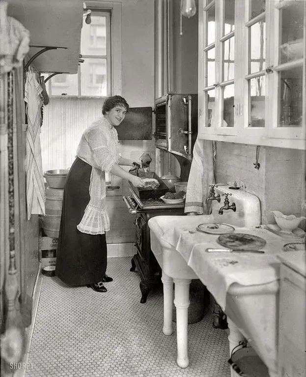 A black and white photo of a woman cooking in a kitchen