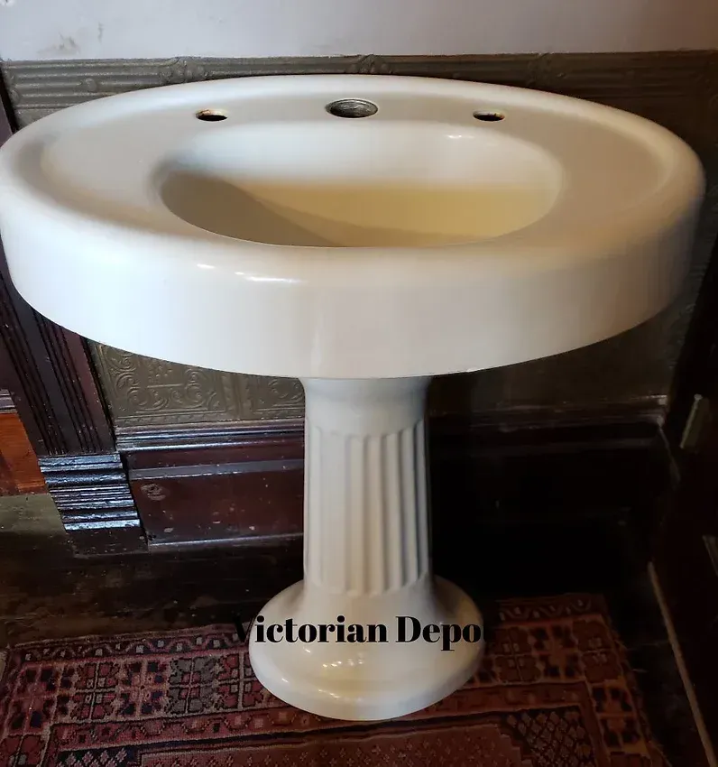 A white pedestal sink is sitting on a rug next to a wall.