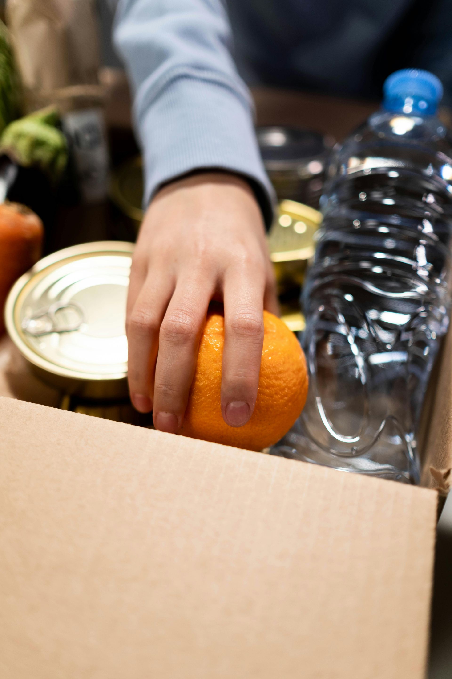 A person is putting an orange in a box of food.