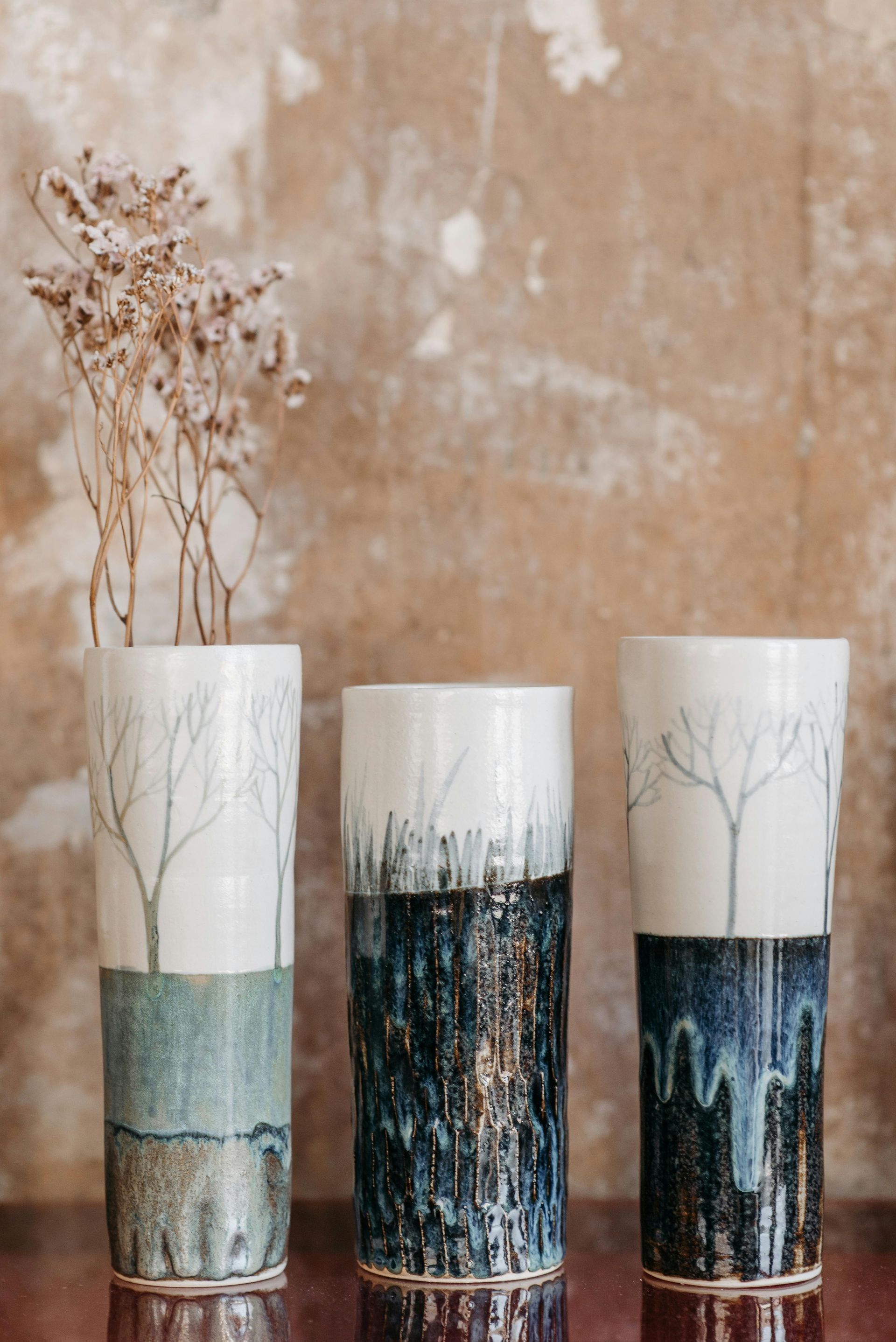 Three vases with trees on them are sitting on a table.